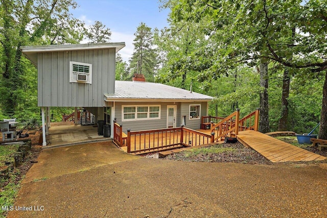 rear view of property with a chimney, a deck, concrete driveway, board and batten siding, and metal roof