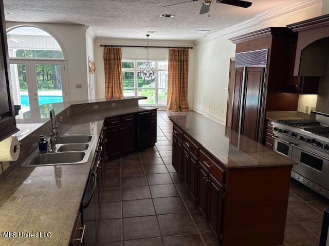 kitchen with dark tile patterned floors, a textured ceiling, a sink, ceiling fan with notable chandelier, and premium appliances
