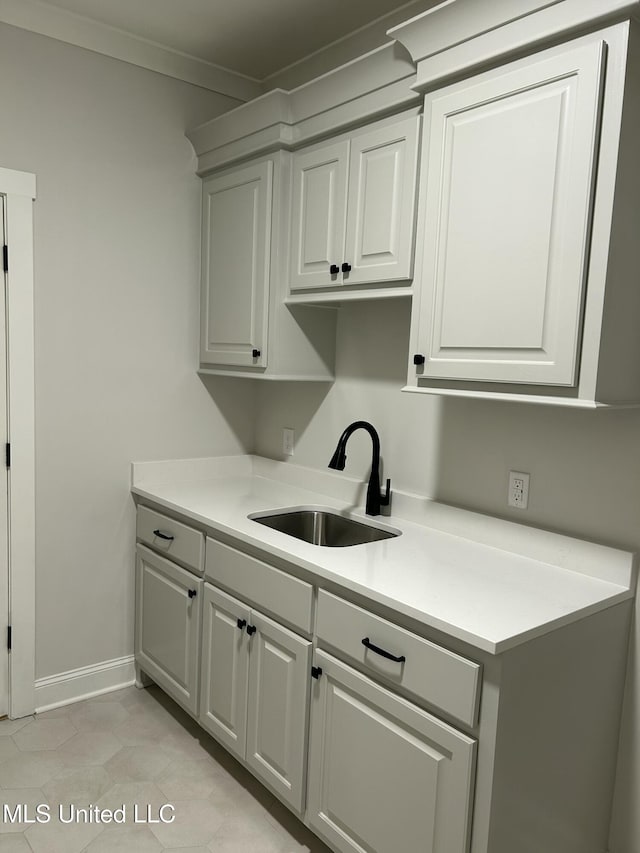 kitchen with crown molding, baseboards, light countertops, white cabinetry, and a sink