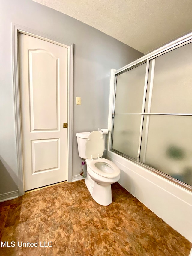 bathroom featuring toilet, combined bath / shower with glass door, and a textured ceiling