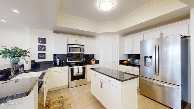 kitchen with appliances with stainless steel finishes, sink, a kitchen island, white cabinetry, and light hardwood / wood-style flooring