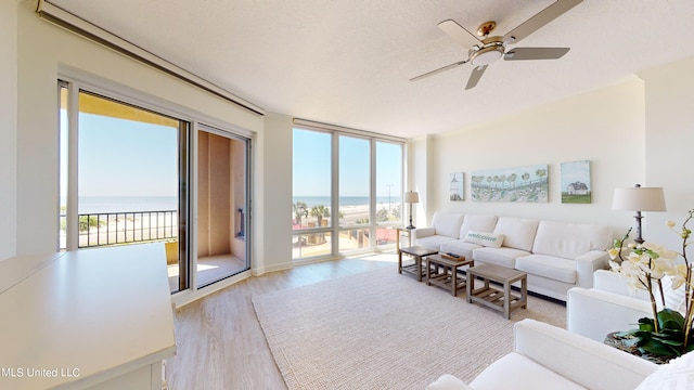 living room featuring a water view, light hardwood / wood-style floors, a textured ceiling, and ceiling fan