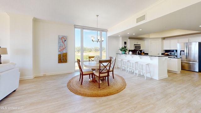 dining area featuring crown molding, a notable chandelier, sink, and light wood-type flooring