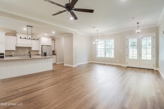 unfurnished living room with sink, crown molding, ceiling fan with notable chandelier, and light wood-type flooring