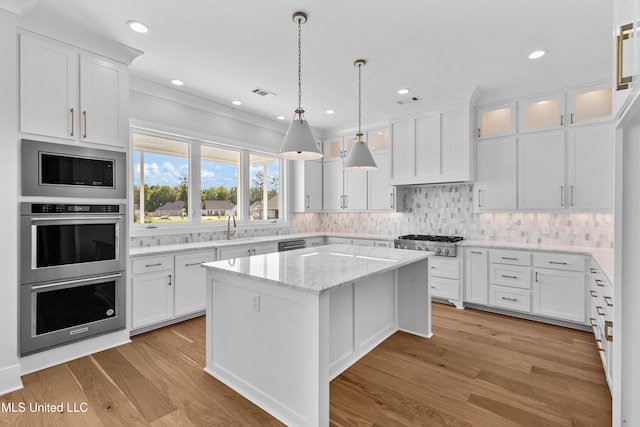 kitchen with white cabinetry, light hardwood / wood-style flooring, light stone countertops, and a center island