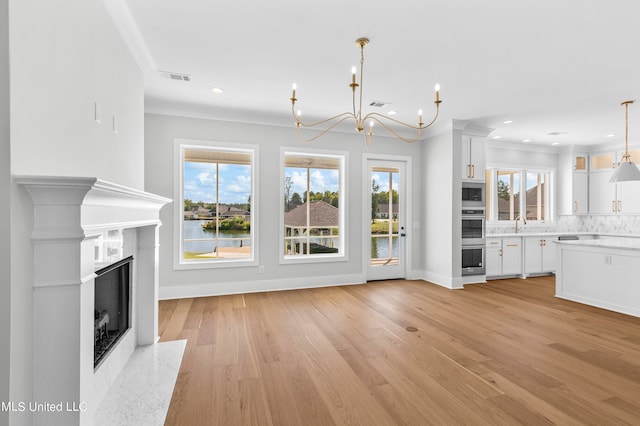 unfurnished living room featuring crown molding, a notable chandelier, a water view, and light hardwood / wood-style floors