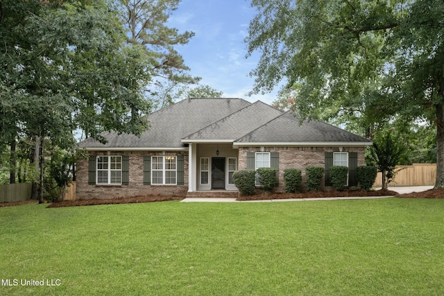 view of front facade featuring a shingled roof, a front yard, fence, and brick siding