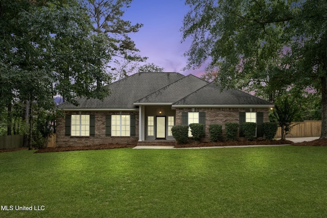 view of front of house with roof with shingles, fence, a lawn, and brick siding