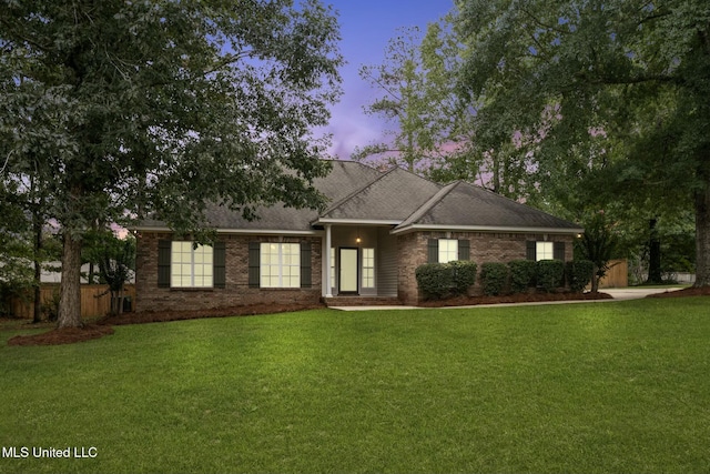 single story home featuring a shingled roof, brick siding, a yard, and fence