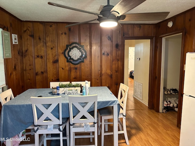 dining area featuring light hardwood / wood-style floors, wood walls, a textured ceiling, and ceiling fan