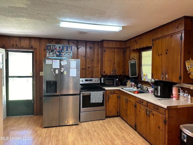 kitchen with wood walls, appliances with stainless steel finishes, sink, a textured ceiling, and light hardwood / wood-style floors