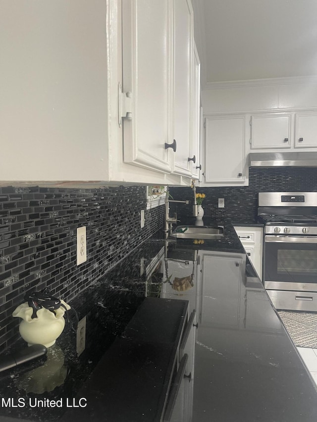 kitchen featuring under cabinet range hood, a sink, white cabinets, tasteful backsplash, and gas stove