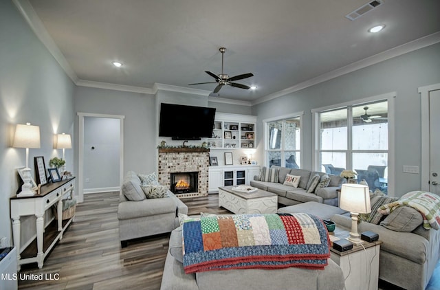 living area with visible vents, ornamental molding, a ceiling fan, wood finished floors, and a brick fireplace