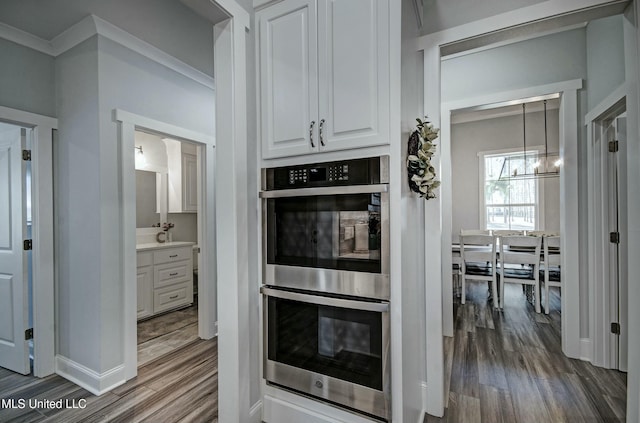 kitchen with wood finished floors, baseboards, ornamental molding, white cabinets, and double oven