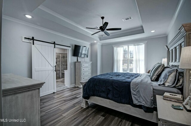 bedroom featuring visible vents, ornamental molding, a tray ceiling, a barn door, and dark wood-style flooring