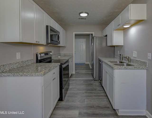 kitchen with white cabinets, appliances with stainless steel finishes, wood finished floors, and a sink