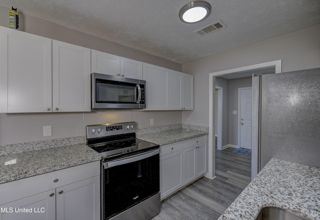 kitchen featuring light stone counters, light wood finished floors, visible vents, stainless steel appliances, and white cabinets
