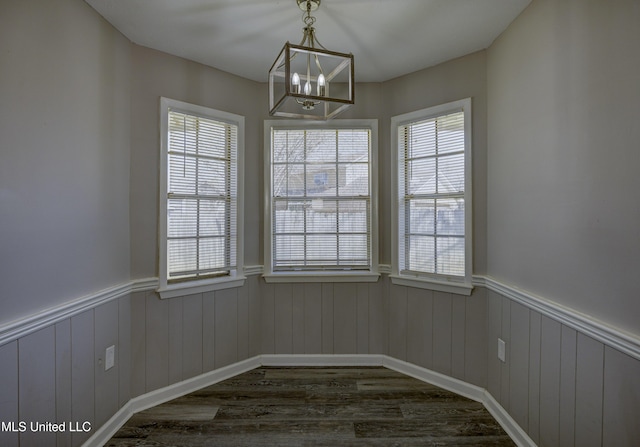 unfurnished dining area with wainscoting, a notable chandelier, dark wood-style floors, and plenty of natural light