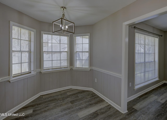 unfurnished dining area with wainscoting, a chandelier, a wealth of natural light, and dark wood-style floors