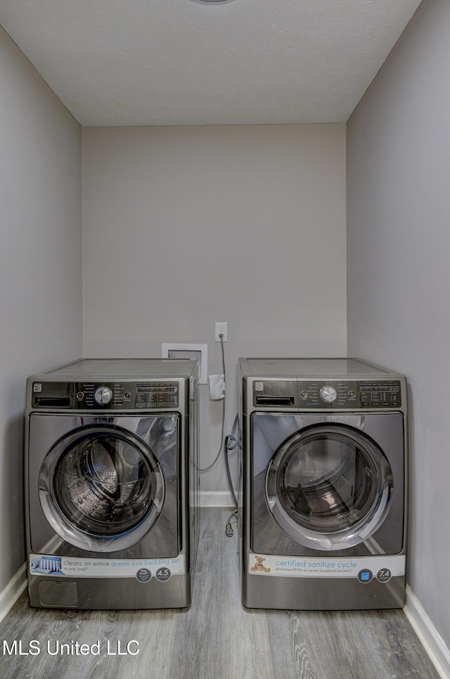 clothes washing area featuring washing machine and clothes dryer, laundry area, baseboards, and wood finished floors