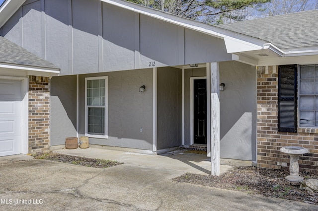 entrance to property with a shingled roof, stucco siding, and brick siding