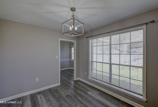 empty room featuring a chandelier, baseboards, and dark wood finished floors