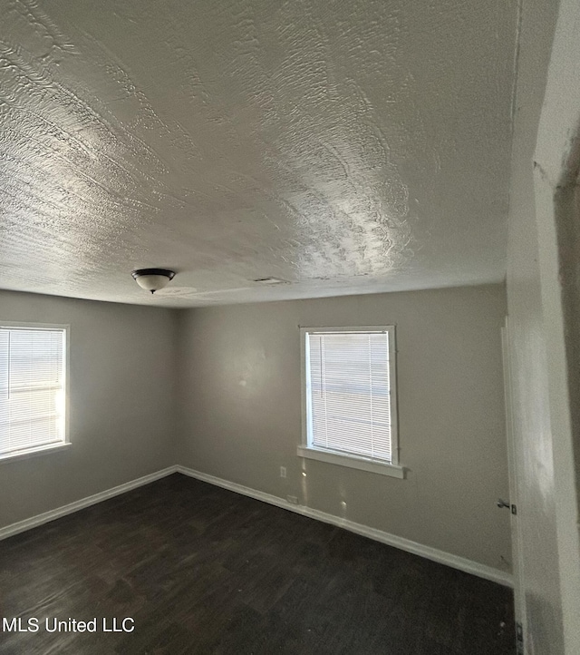 empty room with a textured ceiling, a healthy amount of sunlight, and dark hardwood / wood-style flooring