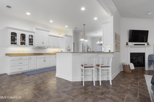 kitchen featuring kitchen peninsula, a kitchen breakfast bar, ornamental molding, decorative light fixtures, and white cabinetry