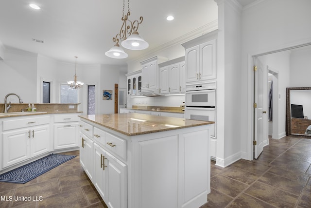 kitchen featuring a center island, sink, double oven, pendant lighting, and white cabinets