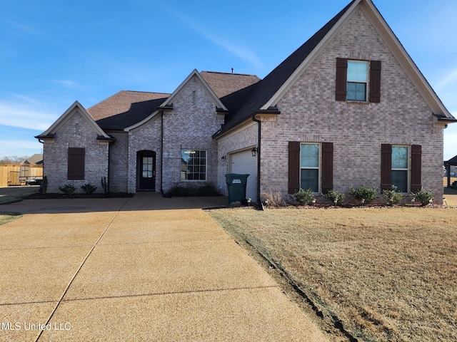 french country home with a garage, driveway, brick siding, and a front lawn