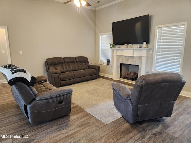 living area with a tile fireplace, wood finished floors, a ceiling fan, baseboards, and ornamental molding