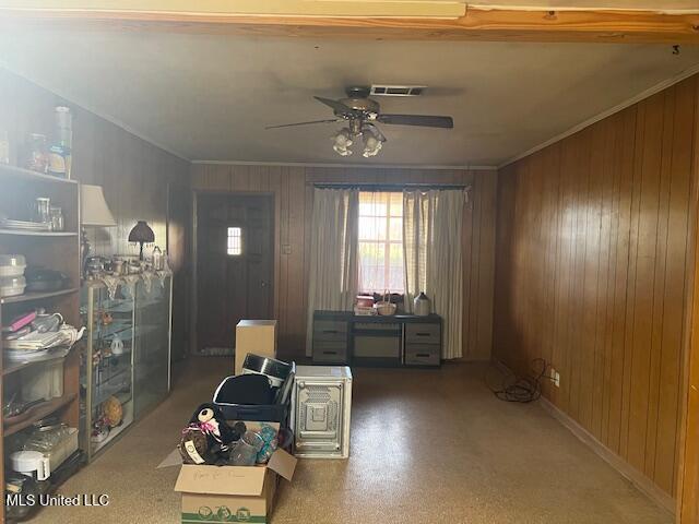 interior space featuring ceiling fan, wooden walls, visible vents, baseboards, and crown molding