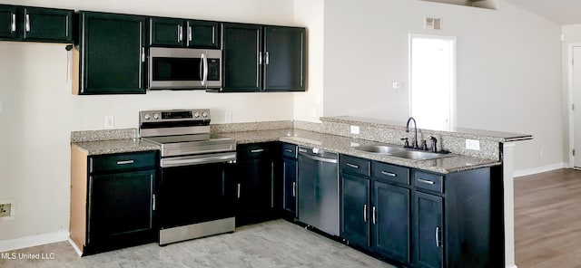 kitchen featuring visible vents, a sink, light stone counters, stainless steel appliances, and a peninsula