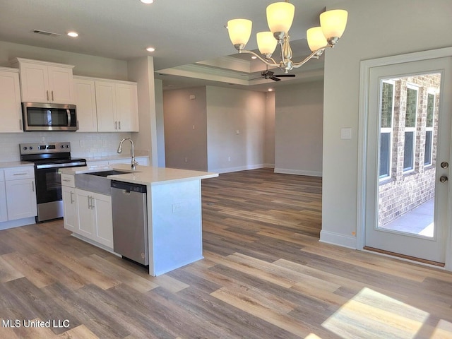 kitchen with white cabinetry, appliances with stainless steel finishes, a kitchen island with sink, and hanging light fixtures