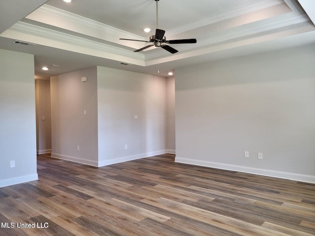 empty room featuring dark wood-type flooring, ceiling fan, ornamental molding, and a raised ceiling