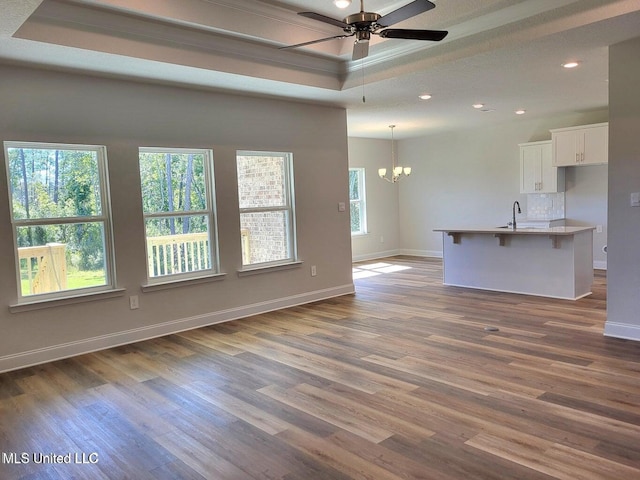 unfurnished living room featuring dark wood-type flooring, a healthy amount of sunlight, a raised ceiling, and ceiling fan with notable chandelier