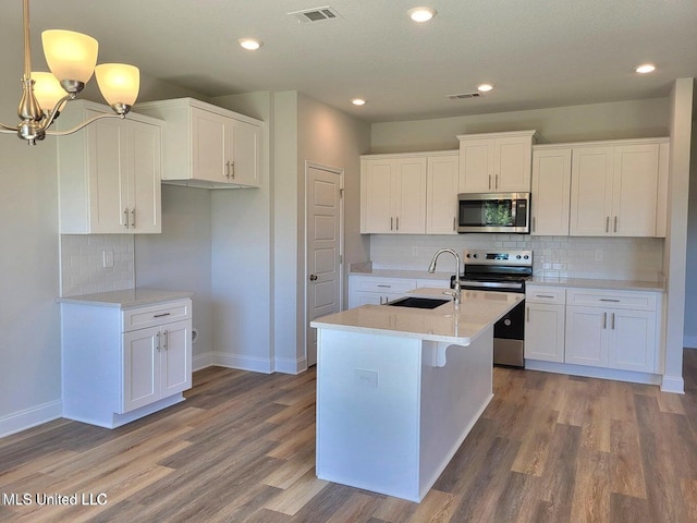 kitchen with appliances with stainless steel finishes, pendant lighting, white cabinetry, sink, and a kitchen island with sink