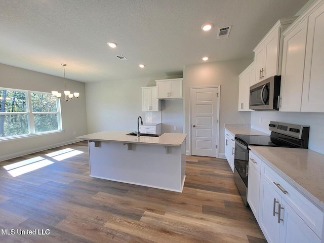 kitchen featuring white cabinetry, a center island with sink, appliances with stainless steel finishes, pendant lighting, and light hardwood / wood-style floors