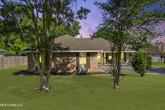 single story home featuring brick siding, roof with shingles, fence, and a yard