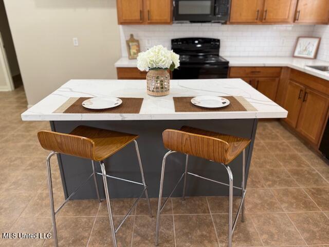 935 Frisky Dr, Brandon, MS 39047 - kitchen with black appliances, a kitchen breakfast bar, decorative backsplash, brown cabinetry, and light countertops