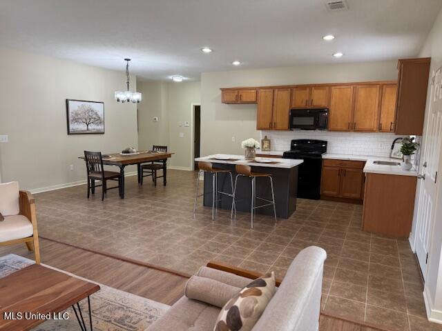 935 Frisky Dr, Brandon, MS 39047 - kitchen featuring black appliances, brown cabinets, a sink, a kitchen island, and tasteful backsplash