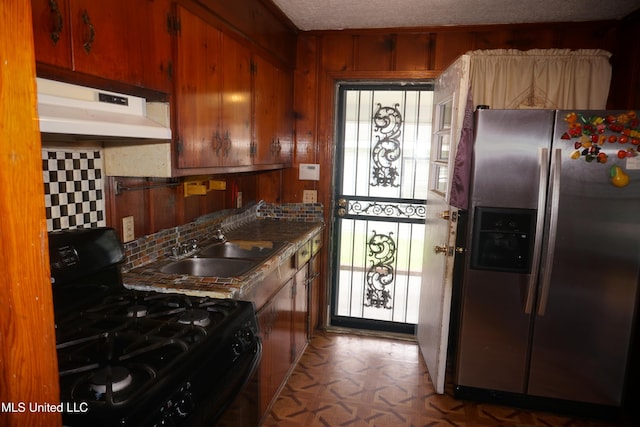 3828 California Ave, Jackson, MS 39213 - kitchen featuring stainless steel fridge, black gas range oven, a sink, under cabinet range hood, and wooden walls