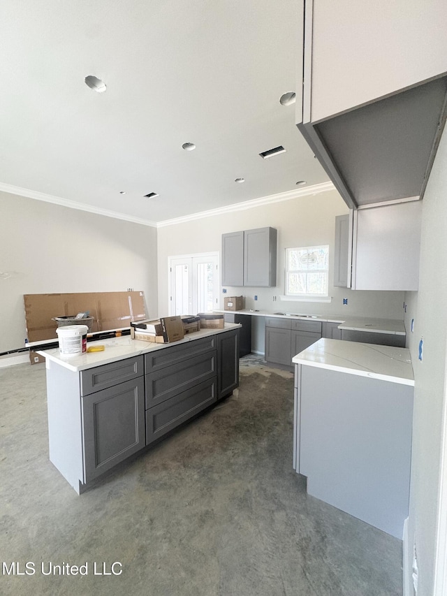 kitchen featuring gray cabinets, light countertops, ornamental molding, a kitchen island, and concrete flooring