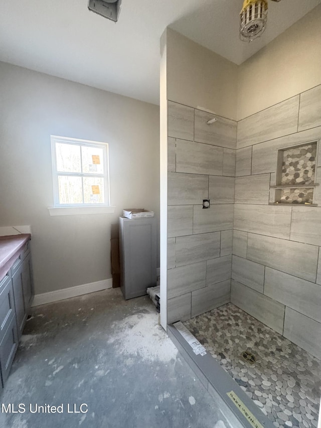 bathroom with unfinished concrete floors, baseboards, and a tile shower