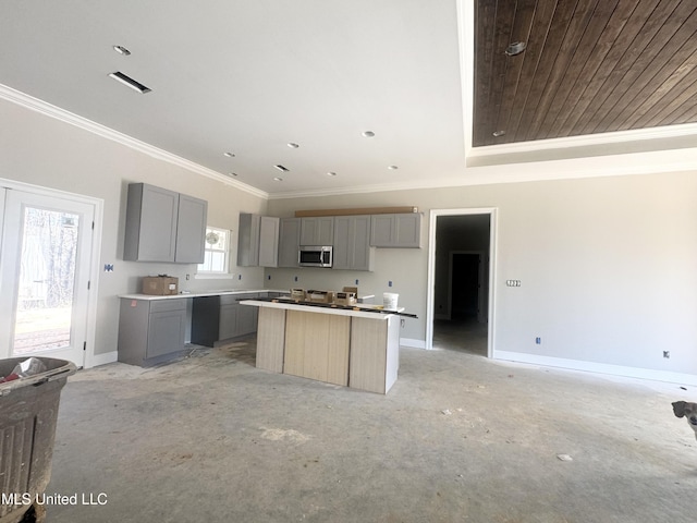 kitchen featuring baseboards, a kitchen island, stainless steel microwave, ornamental molding, and gray cabinets