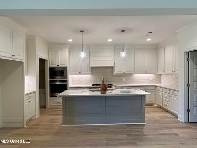 kitchen with light hardwood / wood-style floors, a center island with sink, appliances with stainless steel finishes, white cabinets, and pendant lighting