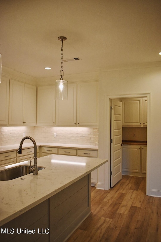 kitchen featuring light stone counters, decorative light fixtures, decorative backsplash, sink, and light hardwood / wood-style flooring