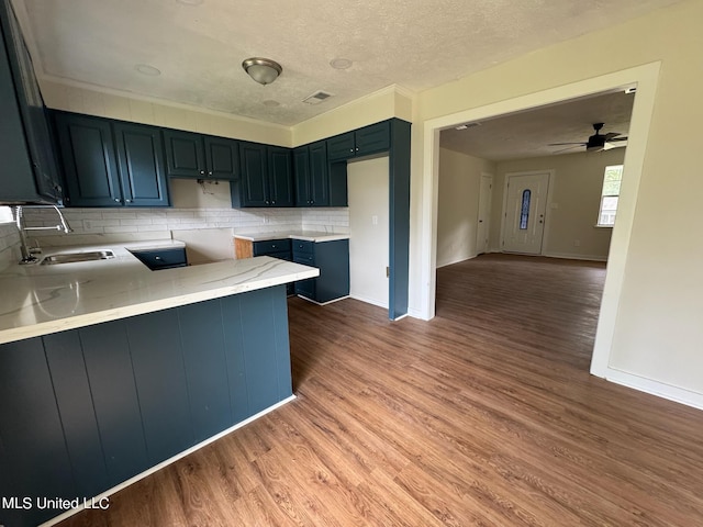 kitchen featuring kitchen peninsula, decorative backsplash, ceiling fan, hardwood / wood-style flooring, and sink