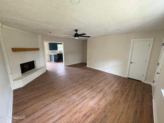 unfurnished living room with dark hardwood / wood-style floors, ceiling fan, a textured ceiling, and a brick fireplace