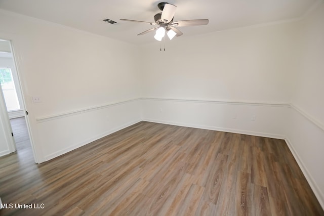 empty room featuring wood finished floors, ornamental molding, a ceiling fan, and visible vents